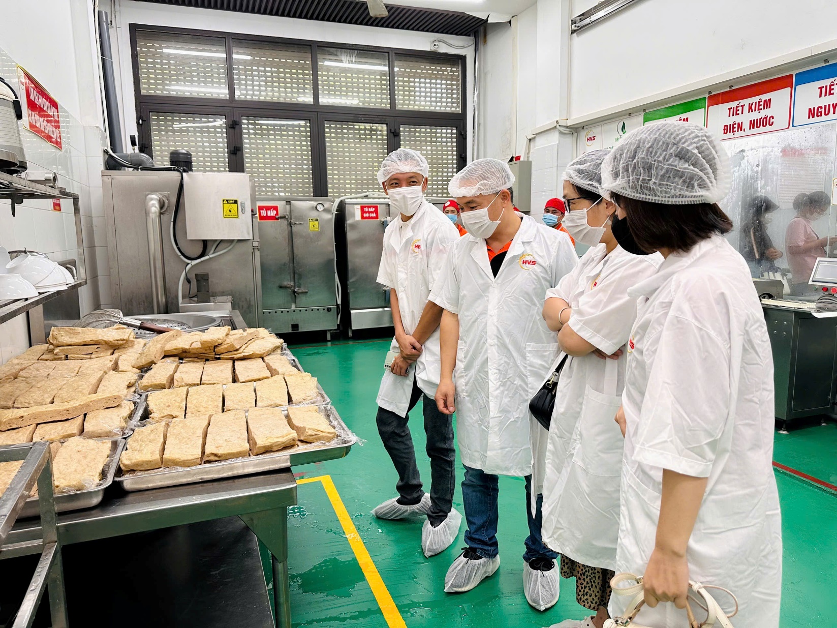 A group of people in white coats and masks standing in a room with trays of food

Description automatically generated