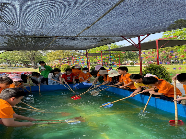 A group of children in orange shirts holding fishing nets in a pond

Description automatically generated