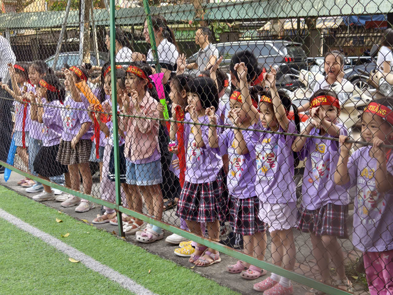 A group of children standing behind a fence

Description automatically generated