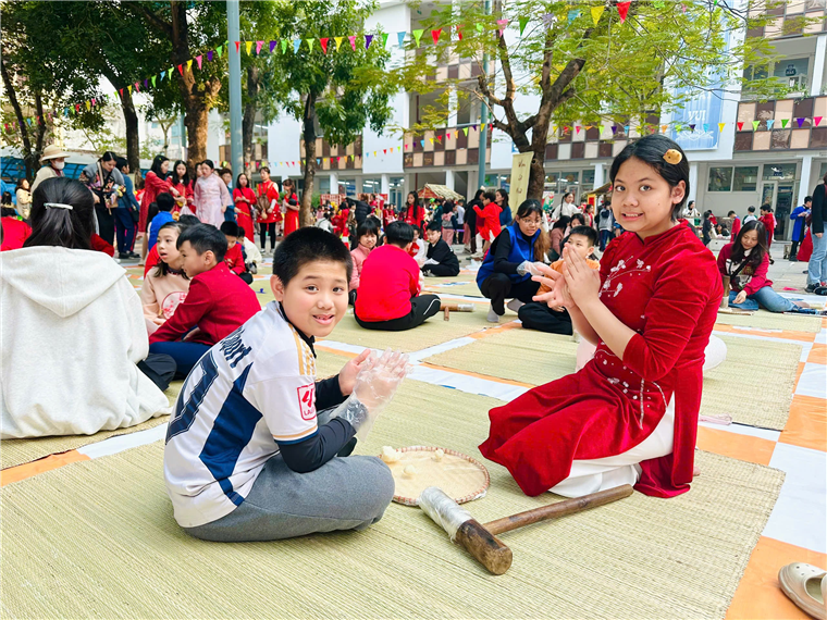 A child and child sitting on a mat with a group of people in the background

Description automatically generated